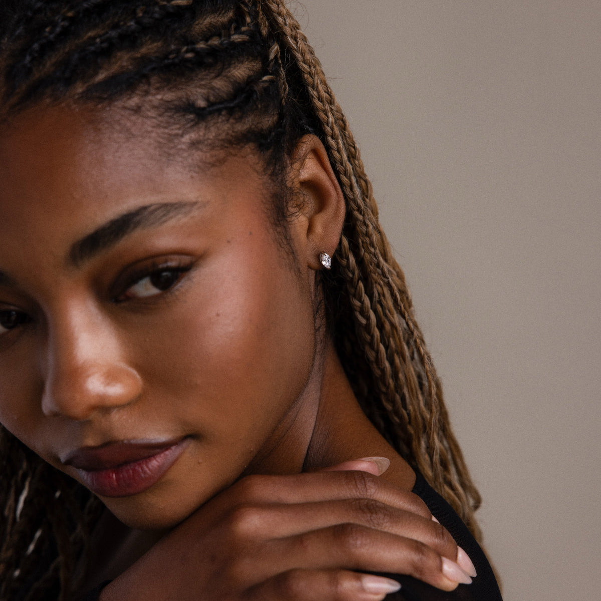 Close-up of a woman with braided hair wearing a silver diamond earring against a neutral background
