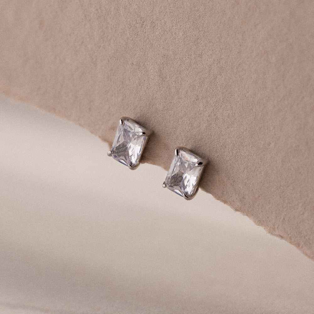 Silver emerald-cut stud earrings on a beige background