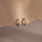 Pair of silver baguette diamond hoop earrings on a beige fabric background