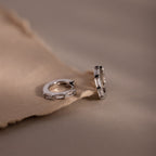 Pair of silver diamond baguette hoop earrings on a soft brown fabric background