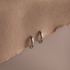 Silver huggie hoop earrings on a beige fabric background