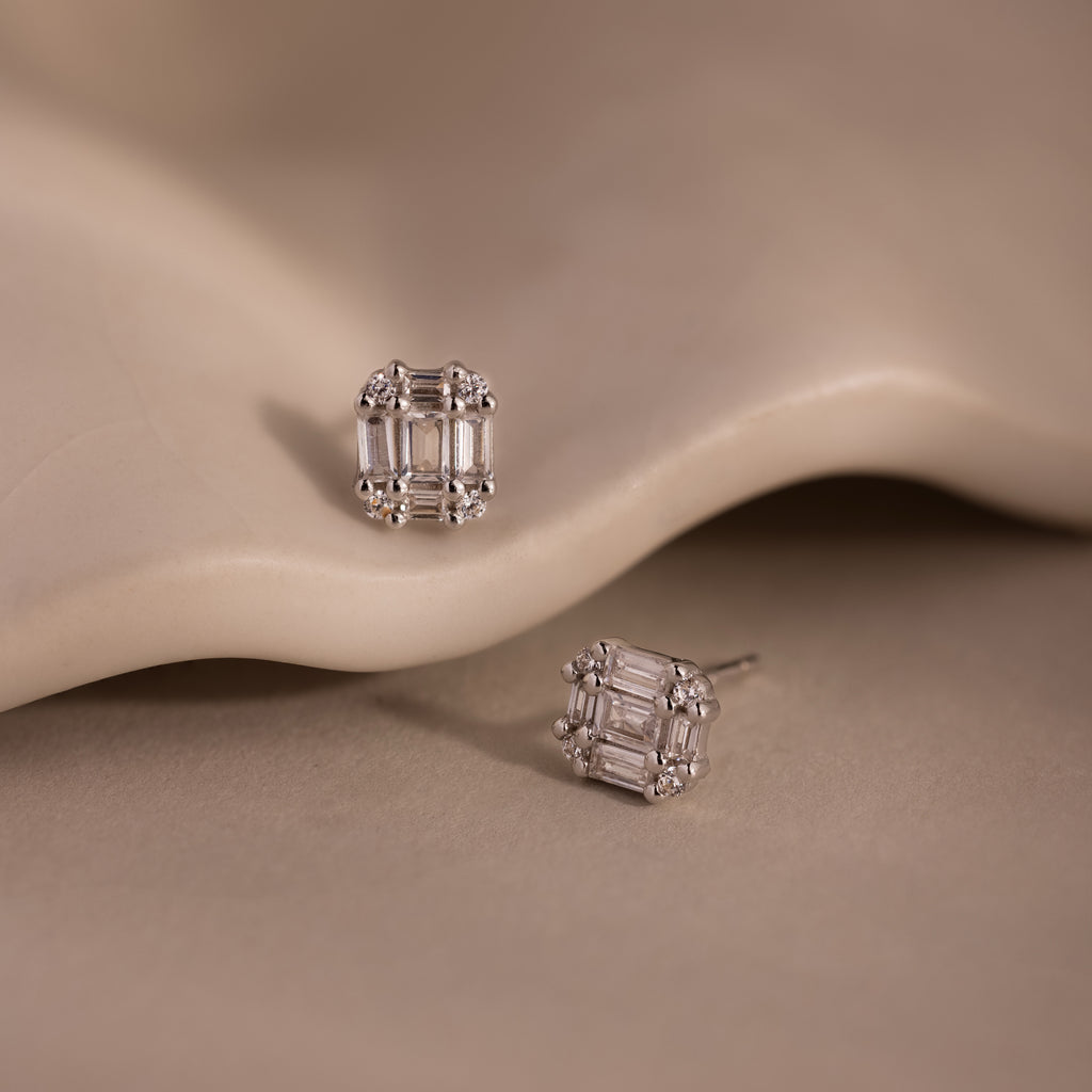 Pair of silver diamond stud earrings on a beige stone background