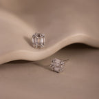 Pair of silver diamond stud earrings on a beige stone background