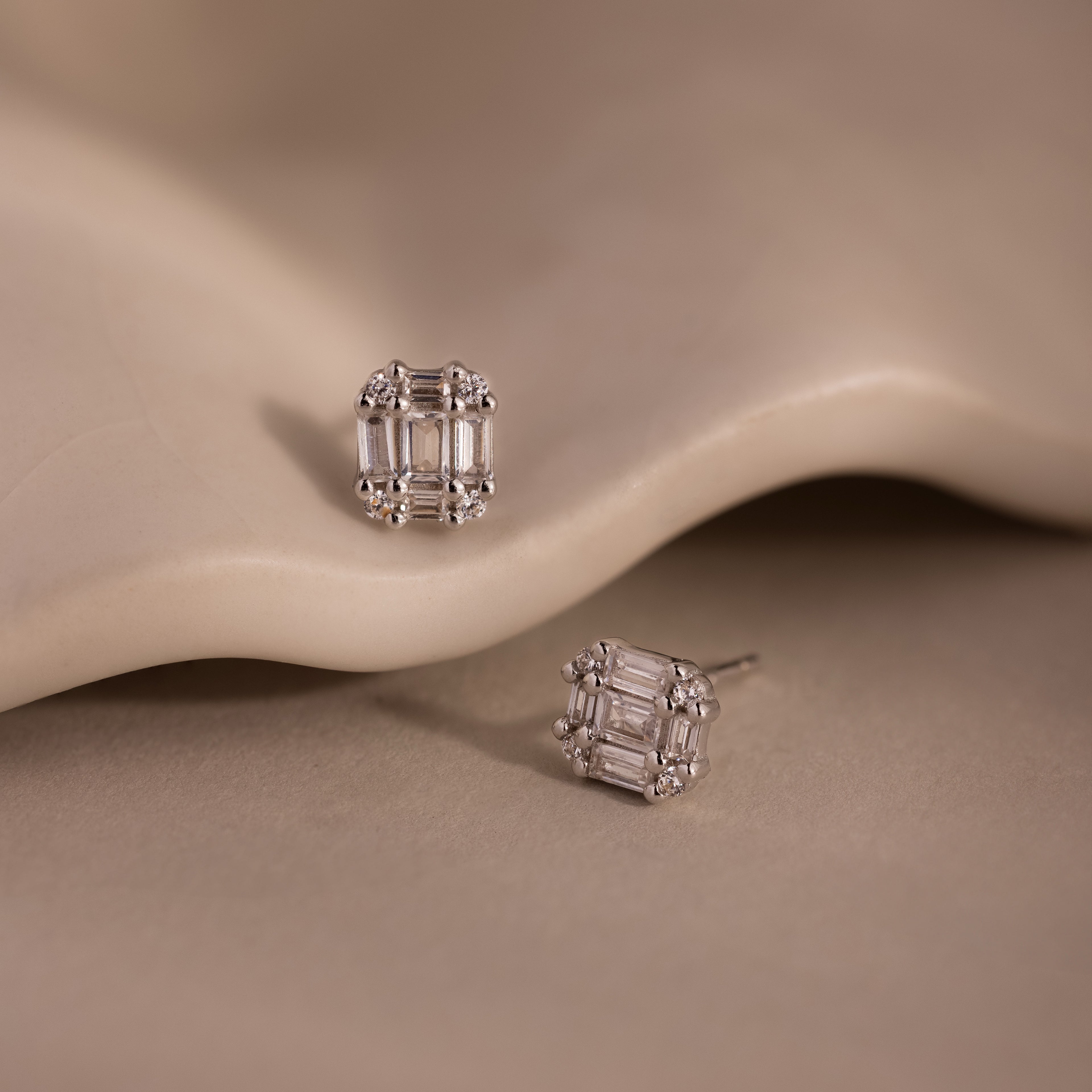 Pair of silver diamond stud earrings on a beige stone background