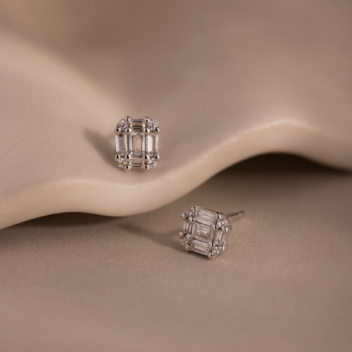 Pair of silver diamond stud earrings on a beige stone background