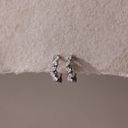 Pair of silver hoop earrings with small clear stones on a textured beige surface