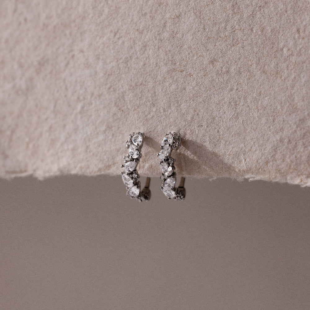 Pair of silver hoop earrings with small clear stones on a textured beige surface
