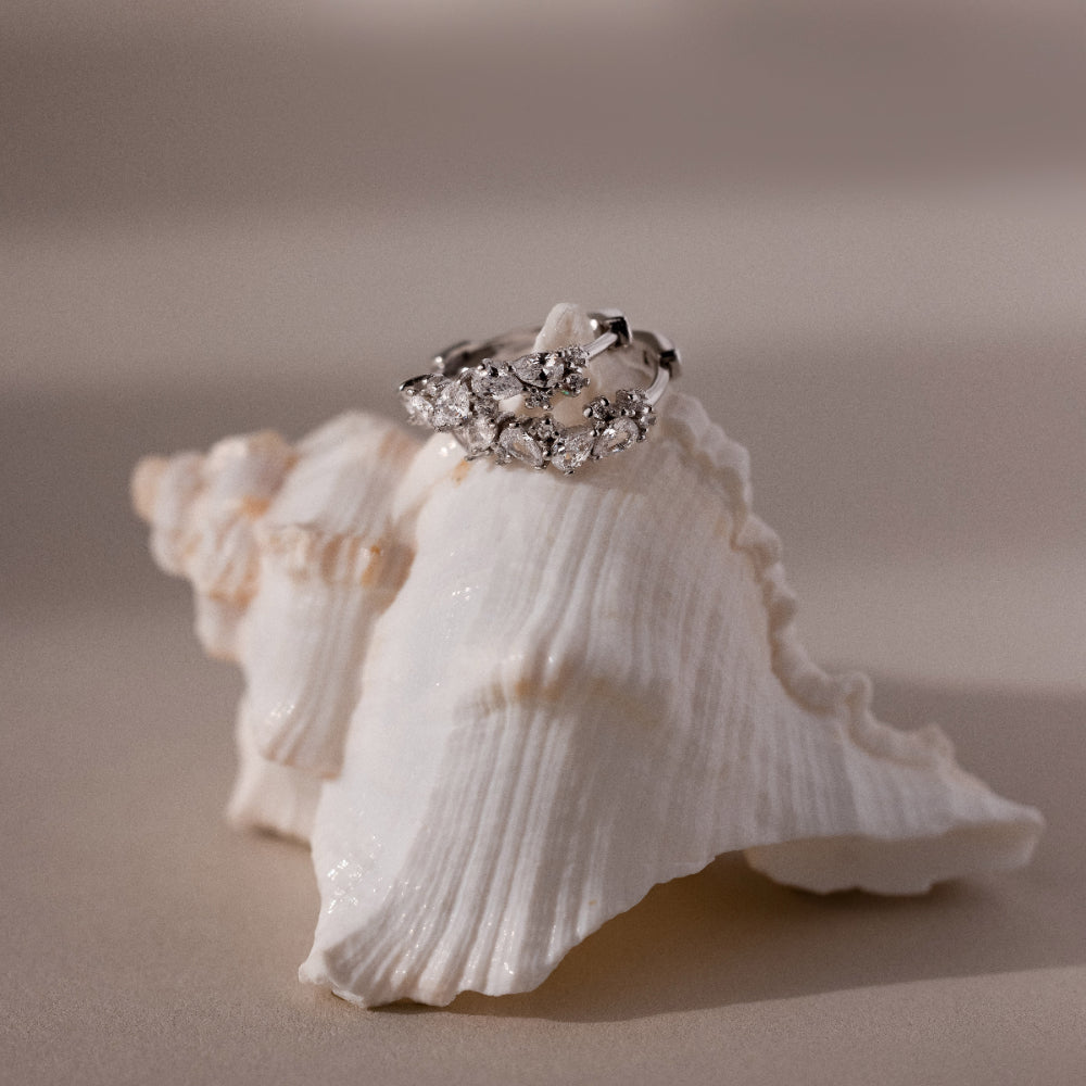 Silver hoop earrings with diamond clusters on a seashell against a beige background