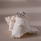Silver hoop earrings with diamond clusters on a seashell against a beige background