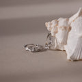 Silver diamond cluster hoop earrings on a sandy surface with a shell in the background