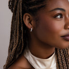 Close-up of a woman with braided hair wearing a silver diamond hoop earring against a neutral background