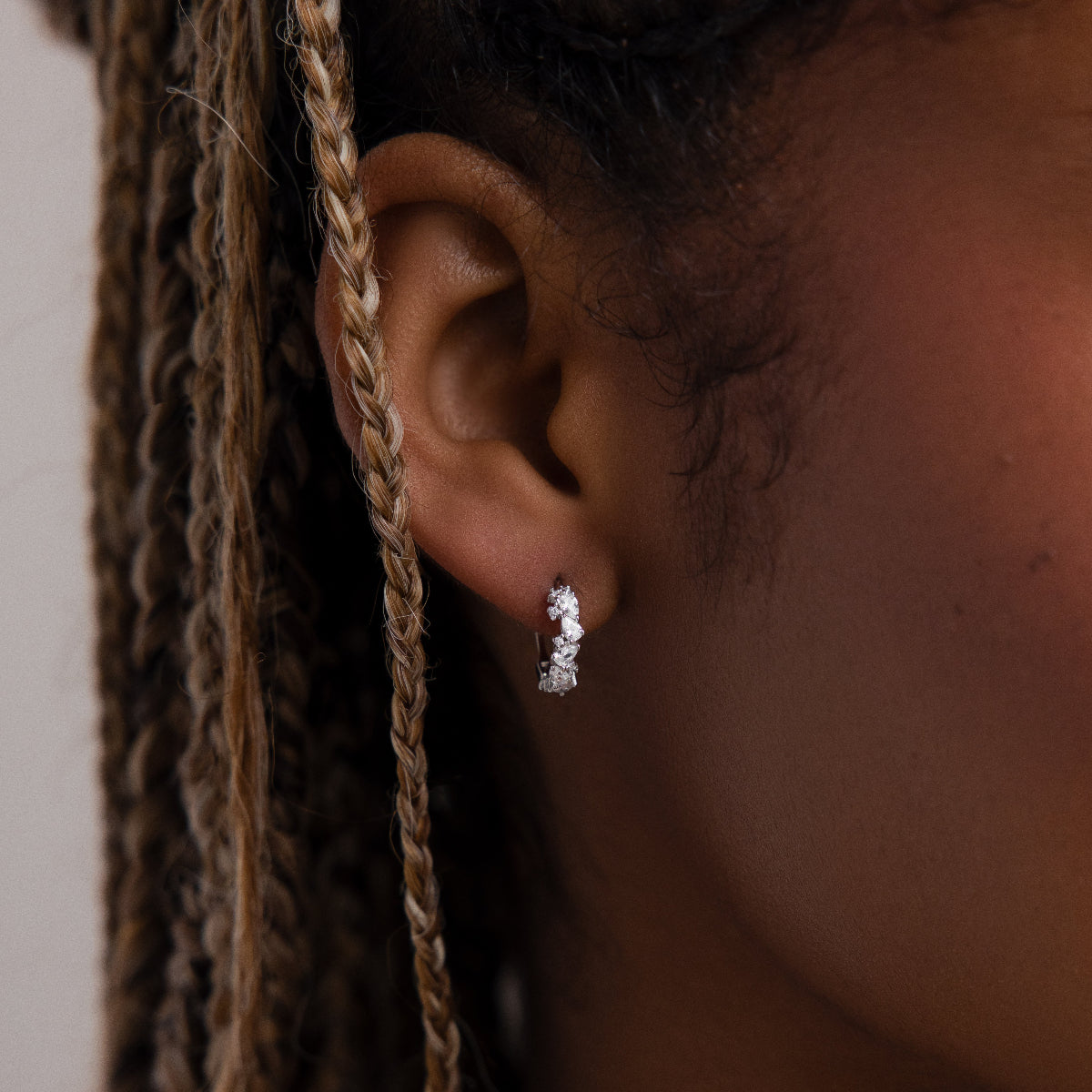 Close-up of a model wearing a silver diamond hoop earring with braided hair.