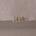 Four dainty diamond cluster huggie hoop earrings, on a textured beige surface