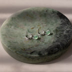 Pair of silver stud hoop earrings with green jade drop pendants on a green stone surface