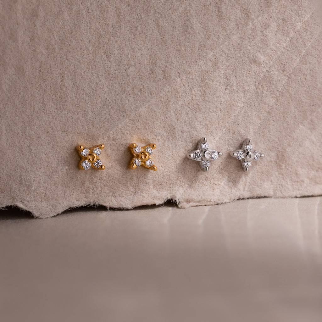 Two pairs of gold and silver star-shaped diamond stud earrings on a textured beige surface