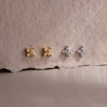 Two pairs of gold and silver star-shaped diamond stud earrings on a textured beige surface