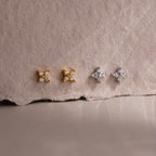 Two pairs of gold and silver star-shaped diamond stud earrings on a textured beige surface