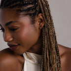Woman with braided hair wearing a silver diamond stud earring and a white top against a neutral background