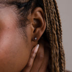 Close-up of a model with a silver dainty diamond earring, hair styled in braids.