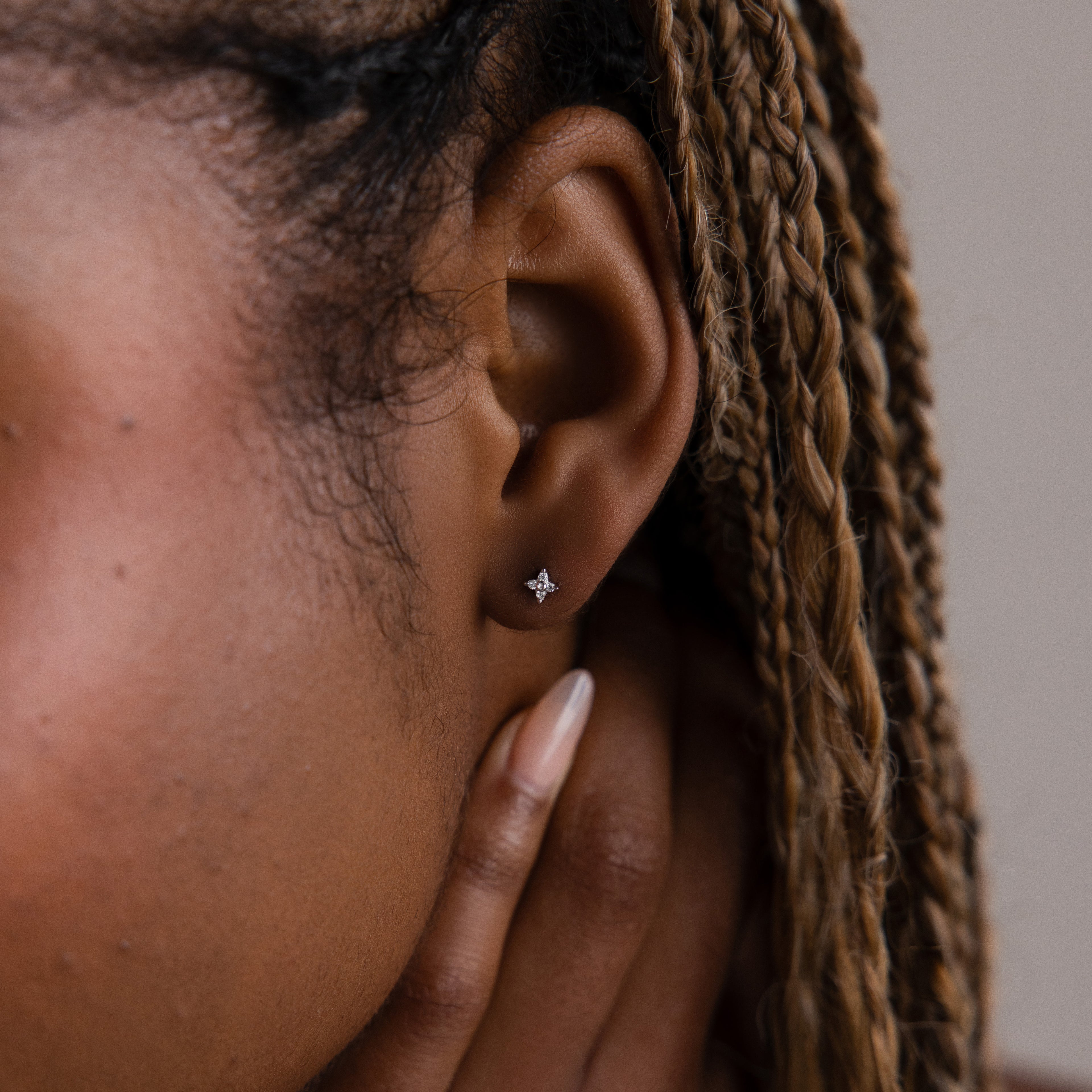 Close-up of a model with a silver dainty diamond earring, hair styled in braids.