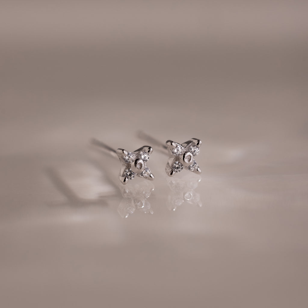 Pair of silver stud earrings with small diamonds on a reflective surface.