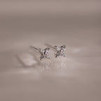 Pair of silver stud earrings with small diamonds on a reflective surface.