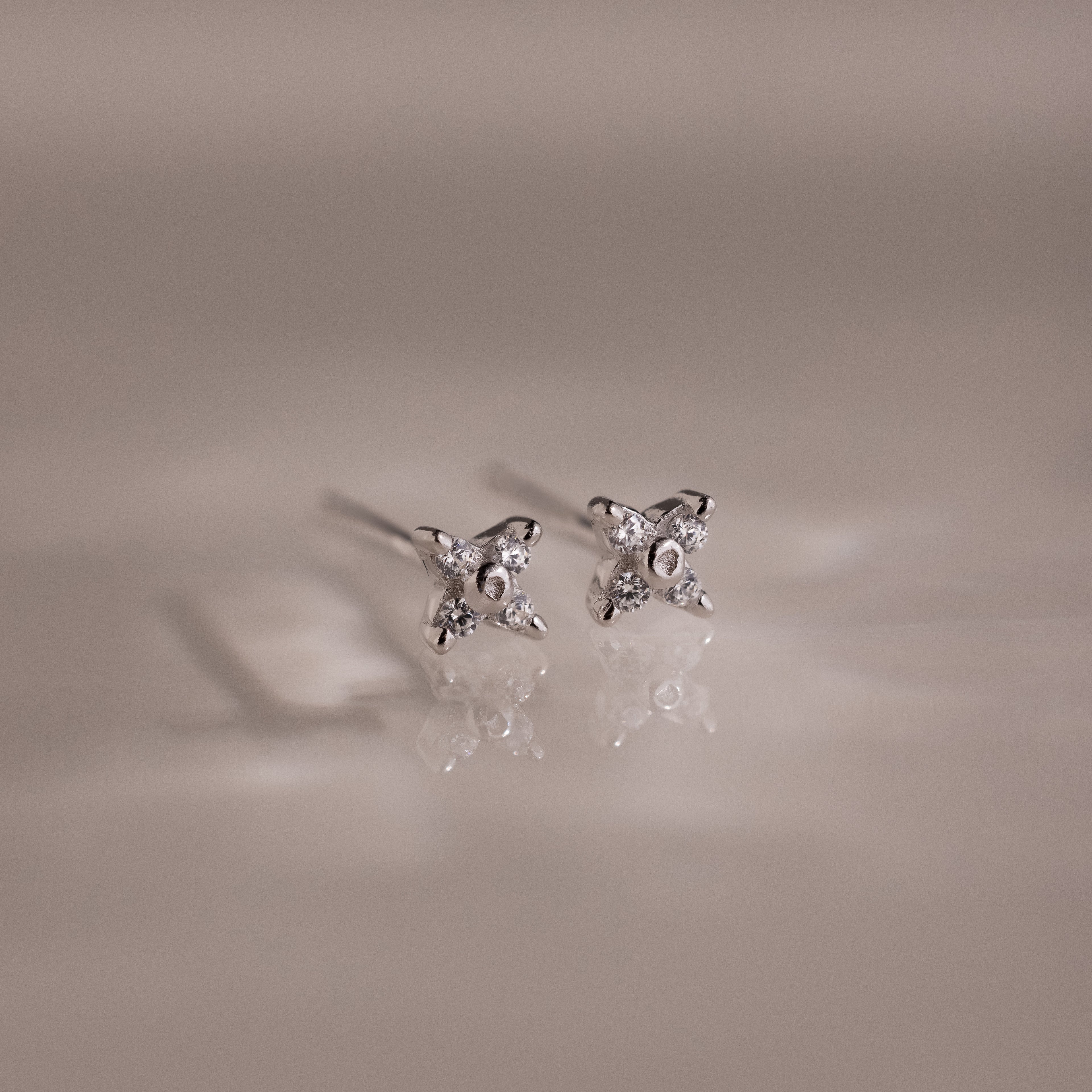 Pair of silver stud earrings with small diamonds on a reflective surface.