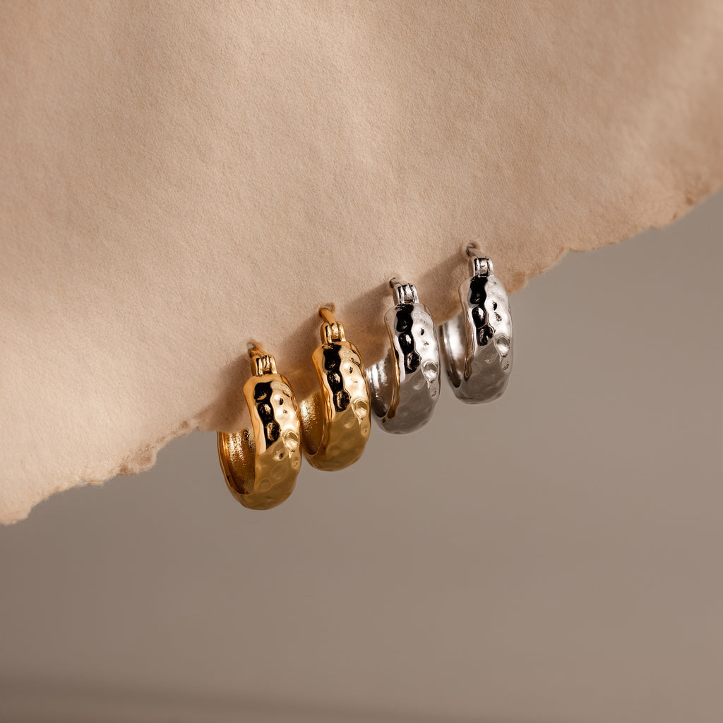 Two pairs of Bold Hammered Huggies in 18K Gold, featuring a textured finish, are displayed on torn paper—perfect minimal design jewelry for everyday style.