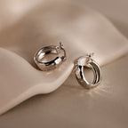 Bold Hammered Huggies with a textured finish rest on a soft, beige surface—ideal for those who love minimalist jewelry.