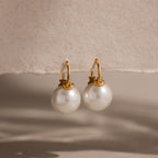 Pearl Dome Drop Earrings showcase lustrous pearls set against a textured beige background with soft shadows.