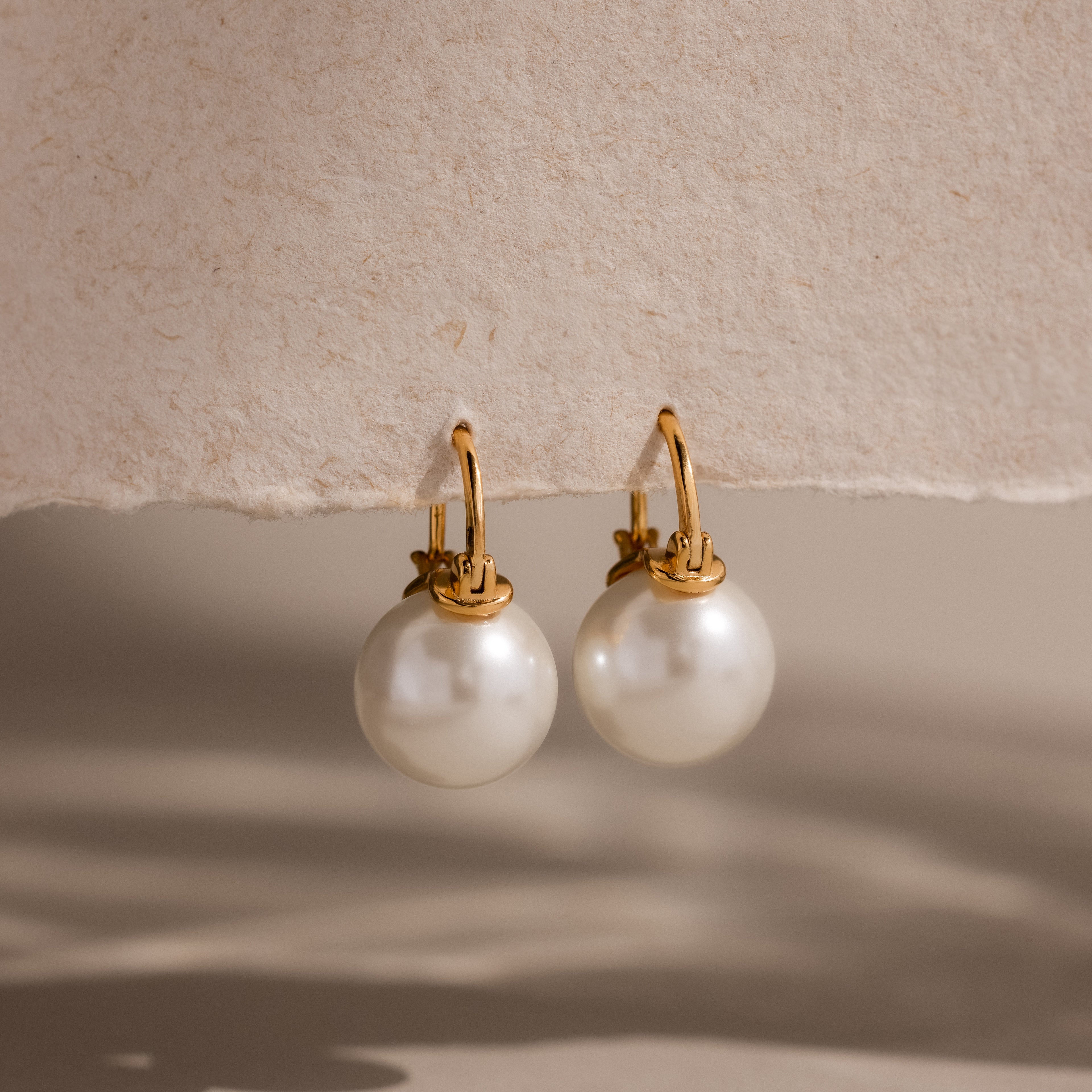 Pearl Dome Drop Earrings showcase lustrous pearls set against a textured beige background with soft shadows.
