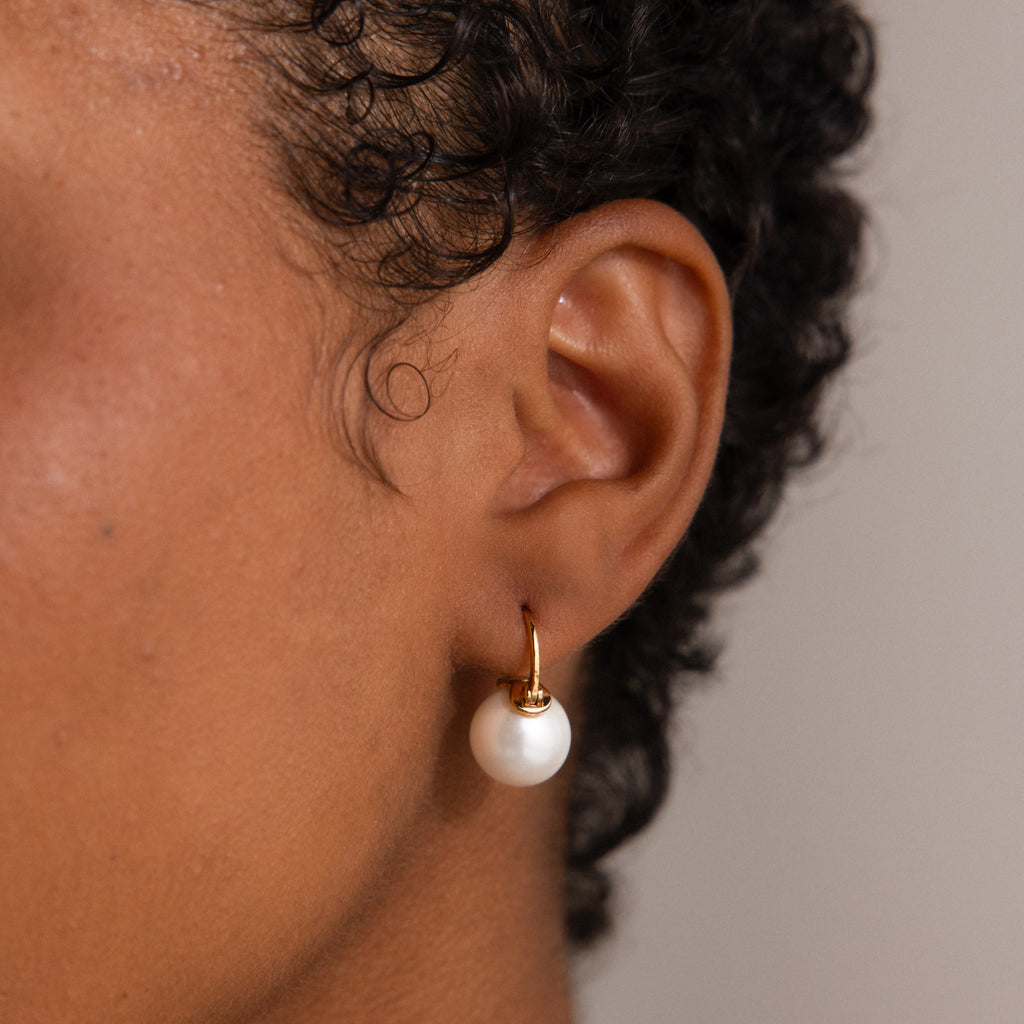 Close-up of an ear adorned with the Pearl Dome Drop Earrings—gold hoops featuring a lustrous pearl pendant for an elegant touch.