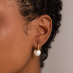 Close-up of an ear adorned with the Pearl Dome Drop Earrings—gold hoops featuring a lustrous pearl pendant for an elegant touch.