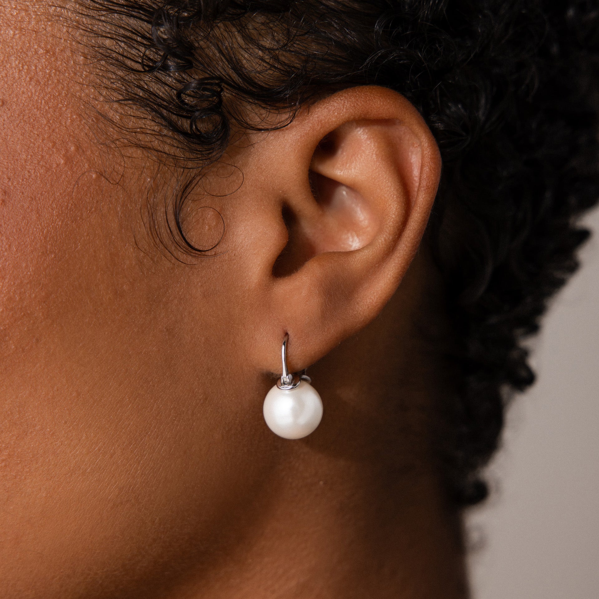 Close-up of a person’s ear adorned with Pearl Dome Drop Earrings in Sterling Silver, featuring lustrous pearls in an elegant and stylish design.