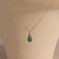 The Jade Drop Necklace, featuring a gold chain and green teardrop jade pendant, is displayed on a beige jewelry bust to highlight its elegant design.