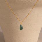 The Jade Drop Necklace, featuring a gold chain and green teardrop jade pendant, is displayed on a beige jewelry bust to highlight its elegant design.