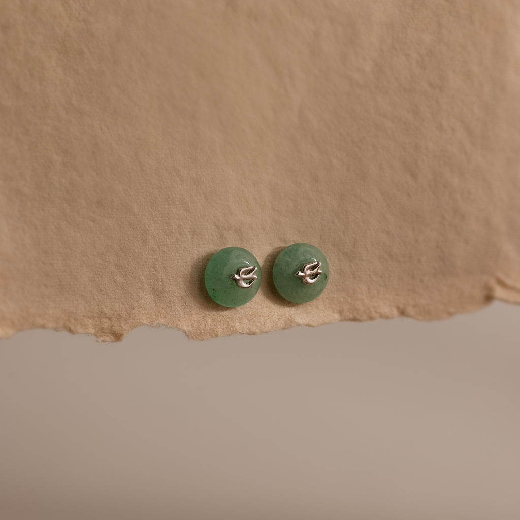 Silver Jade Bird Studs with dainty silver dove birds on round green jade discs, displayed on a neutral paper surface.