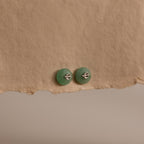 Silver Jade Bird Studs with dainty silver dove birds on round green jade discs, displayed on a neutral paper surface.