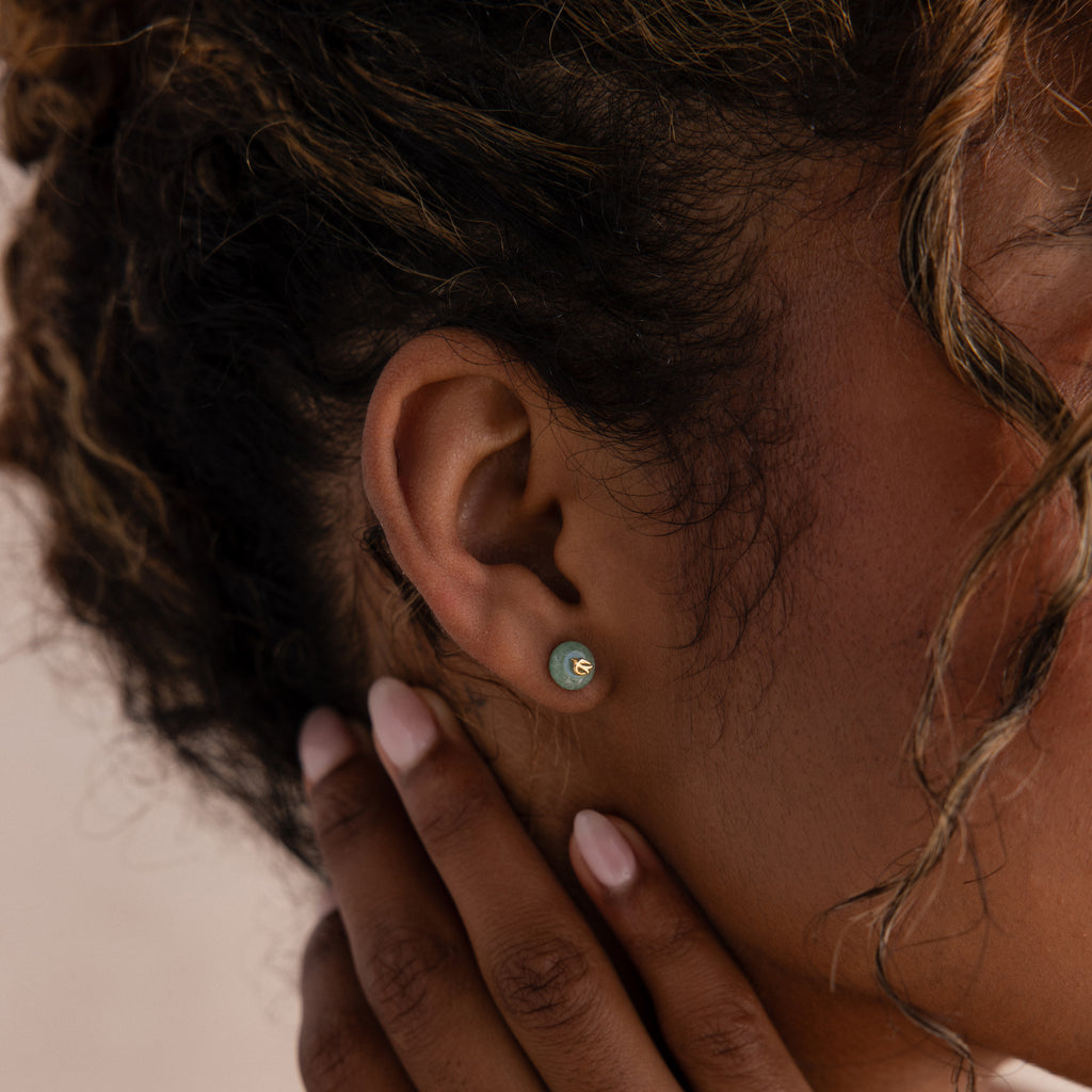 Model wearing gold Jade Bird Studs with dainty golden dove birds on round green jade discs.