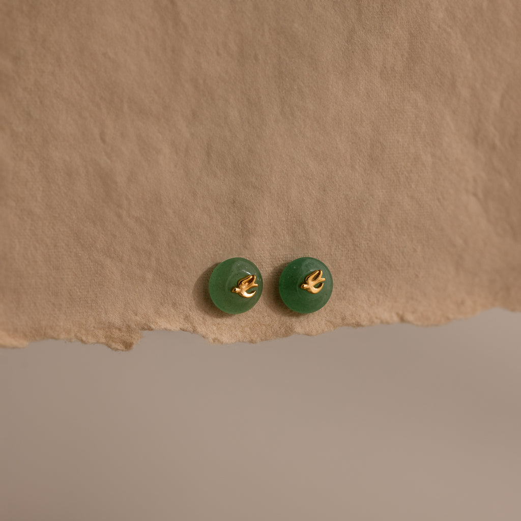 Gold Jade Bird Studs with dainty golden dove birds on round green jade discs, displayed on a neutral paper surface.