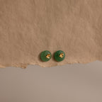 Gold Jade Bird Studs with dainty golden dove birds on round green jade discs, displayed on a neutral paper surface.