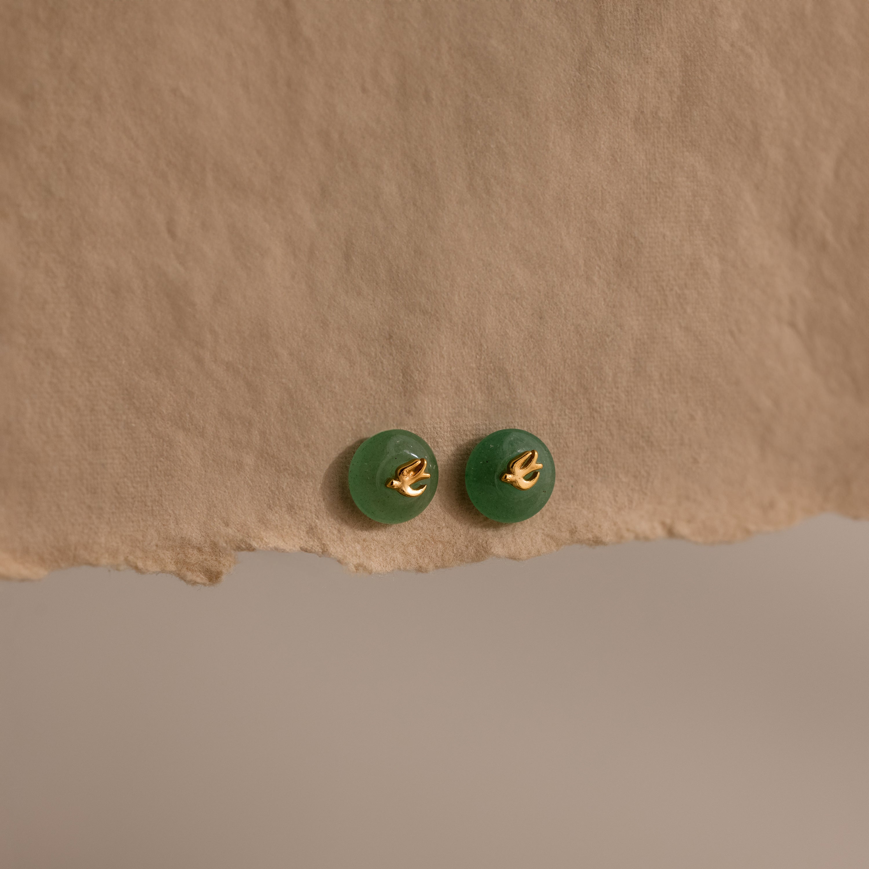 Gold Jade Bird Studs with dainty golden dove birds on round green jade discs, displayed on a neutral paper surface.