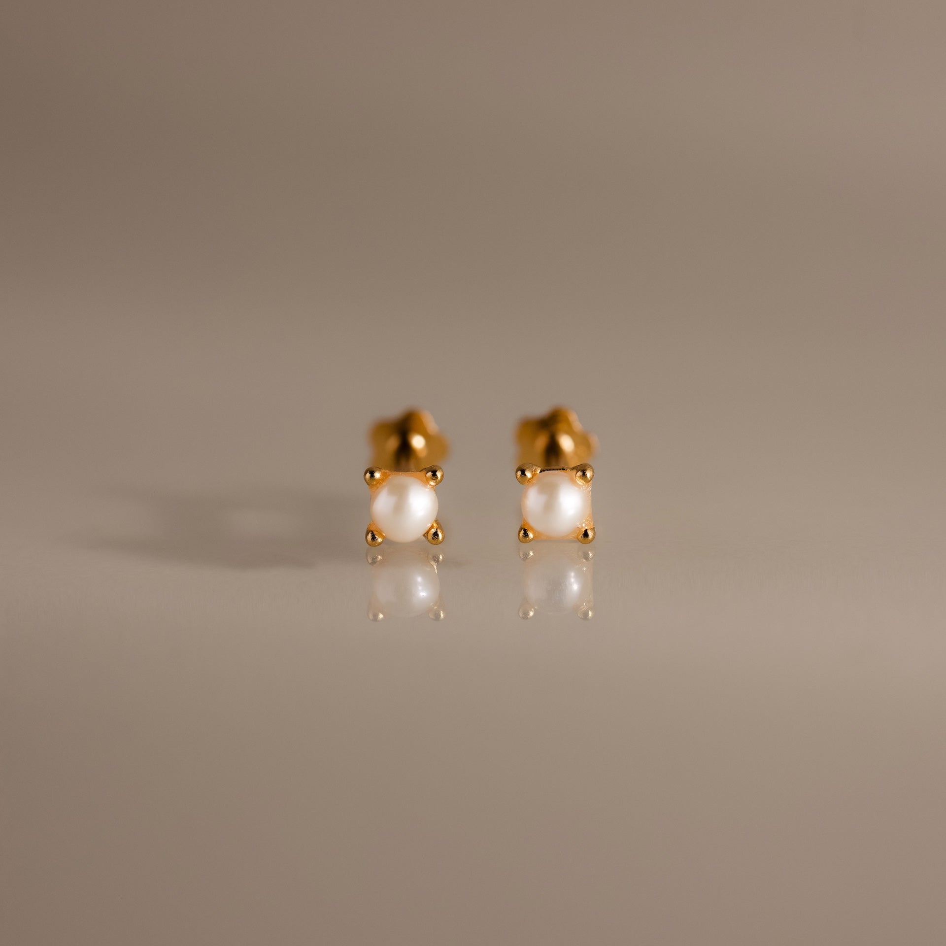 Baby Venus Flatback Studs: Elegant pearl stud earrings featuring gold floral backings and lustrous white pearls, displayed on a smooth, neutral surface.
