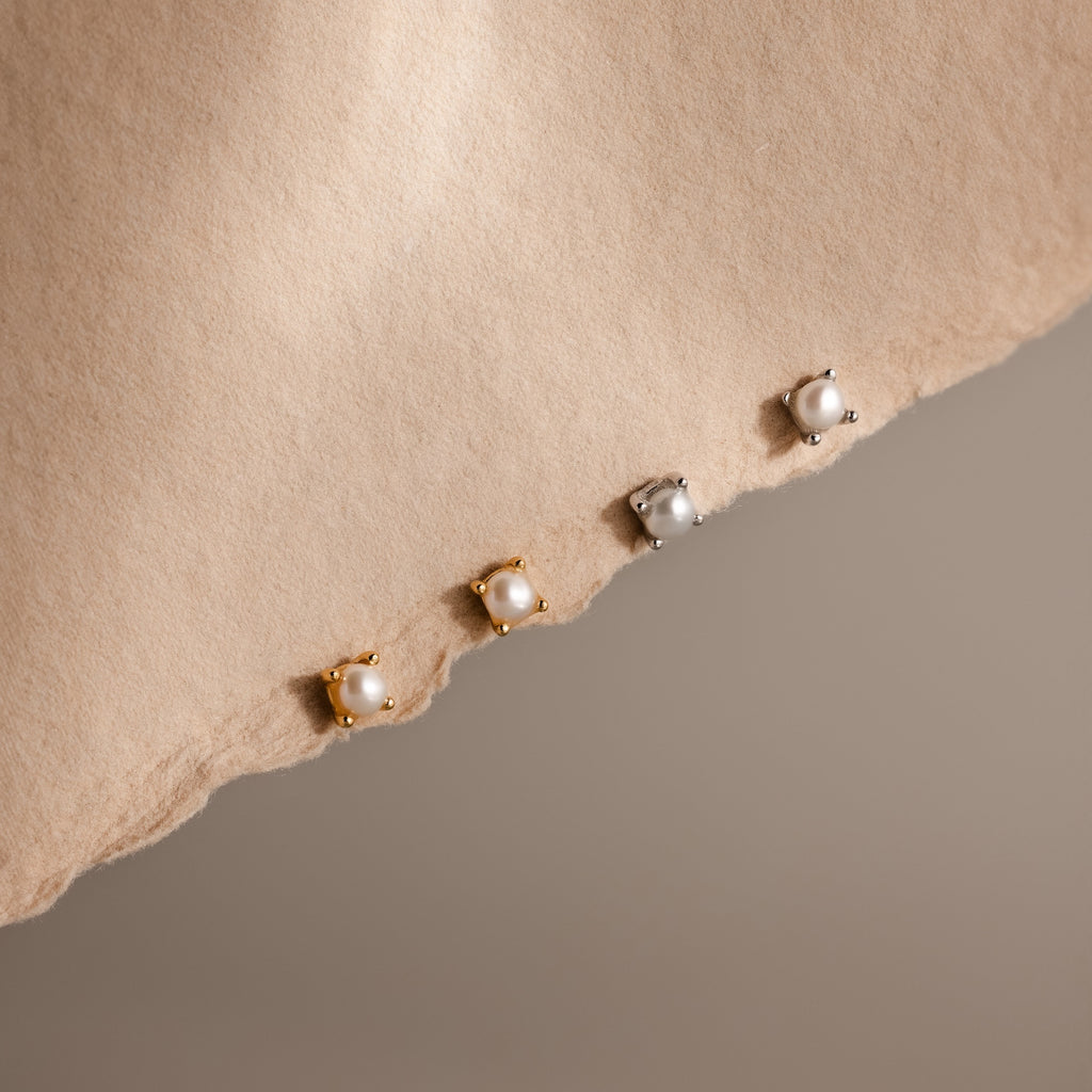 Three pairs of Baby Venus Flatback Studs—two gold, one silver—rest on a torn beige paper background, creating an elegant jewelry set with timeless charm for any look.