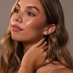 Woman with long wavy hair and glowing skin wears Baby Venus Flatback Studs, featuring a floral backing, as she looks upward with her hand near her neck.