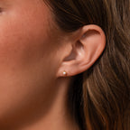 Close-up of a womans ear wearing Baby Venus Flatback Studs in 18K Gold with a floral backing, her light brown hair softly framing the delicate pearls.