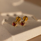 Elegant Garnet Flatback Studs with red gemstones, these gold earrings add a dainty touch and look stunning against a textured, light-colored surface.