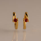 Floating Garnet Huggies: Twisted gold hoop earrings with a wavy design, each featuring a round garnet center—perfect personalized jewelry for birthstone lovers.
