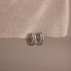 Ribbed Pave Huggies in Sterling Silver, featuring a textured, chunky hoop design, are displayed on a soft cream-colored fabric background.