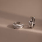 Two Ribbed Pave Huggies in Sterling Silver, featuring a row of sparkling stones, are displayed on a beige background.